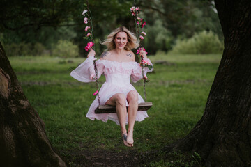 Woman in a Flowing Pink Dress Sitting on a Floral Swing in Nature