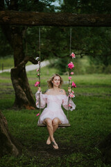 Woman in a Flowing Pink Dress Sitting on a Floral Swing in Nature