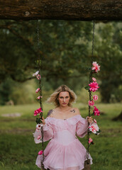 Woman in a Flowing Pink Dress Sitting on a Floral Swing in Nature
