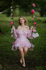 Woman in a Flowing Pink Dress Sitting on a Floral Swing in Nature