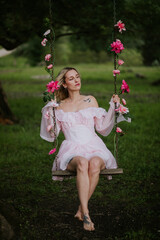 Woman in a Flowing Pink Dress Sitting on a Floral Swing in Nature