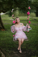 Woman in a Flowing Pink Dress Sitting on a Floral Swing in Nature