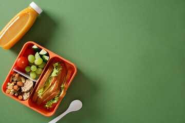 Healthy school lunch box. Top view of bento box with sandwich, fruits, nuts, and juice on green...