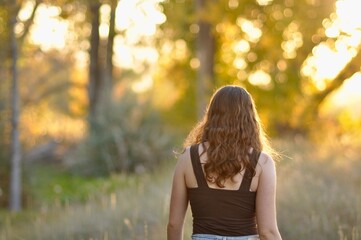Naklejka premium Woman in nature setting with trees walking away at sunset