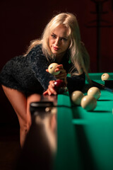 Young beautiful blonde girl in a studio with a billiard table. Photographed in low key.