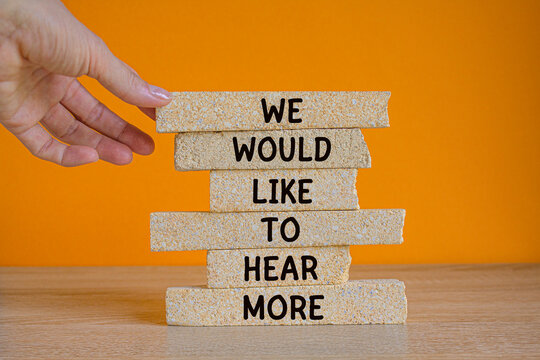 We would like to hear more symbol. Brick blocks with words We would like to hear more. Beautiful orange background. Businessman hand. Business concept.