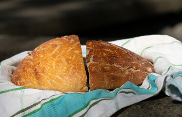 Close-up of two half and fresh loaves of bread lying on a kitchen towel. The bread is photographed outdoors.