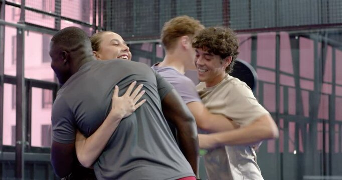 Group of diverse friends enjoying padel tennis on indoor court, smiling and holding rackets