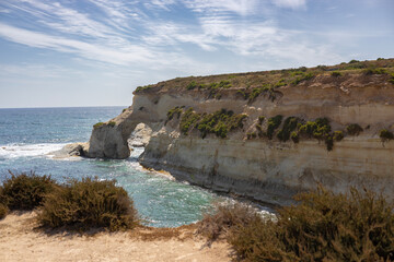 Beautiful Maltese coast with unique rock formations and arches, traditional salt panes and turquoise blue water near St Peter's Pool.