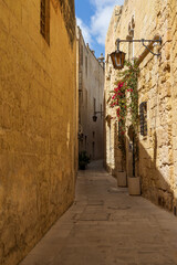 Obraz premium Narrow alleyway in the old city of Mdina with traditional lanterns, ragged limestone houses and tranquil atmosphere, Maltese Islands.