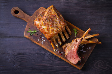 Roasted rack of lamb. Lamb chops on serving board and black wooden background. High angle view