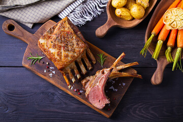 Roasted rack of lamb. Lamb chops on serving board and black wooden background. High angle view