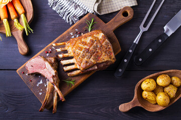 Roasted rack of lamb. Lamb chops on serving board and black wooden background. High angle view