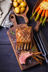 Roasted rack of lamb. Lamb chops on serving board and black wooden background. High angle view
