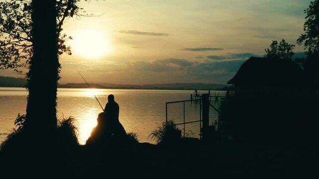 Ein Mann sitzt ruhig am See und fischt, w&auml;hrend die Sonne langsam untergeht. Goldene Reflexe tanzen auf dem Wasser &ndash; ein stiller Moment voller Frieden, Natur und abendlicher Magie.