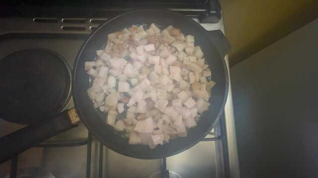 Close-up video of raw pork fat cubes slowly rendering in a hot frying pan. Traditional method of lard preparation, showing bubbling fat and sizzling pieces of pork.