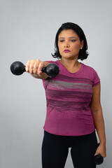 Fit brunette woman performing weight lifting with dumbbell at studio, wearing athletic outfit. She has a focused expression, ideal for workout, healthy lifestyle, strength training. Copy space.