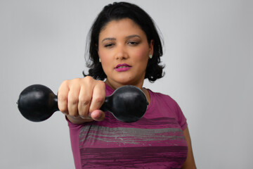 Close up of brunette woman performing weight lifting with dumbbell at studio. Horizontal portrait ideal for workout, fitness, strength training. Gray background, copy space, focus on foreground.