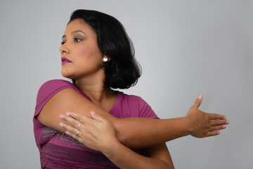 Pretty, serious woman stretching out her arm. Ideal for home workout, exercising, warm-up and fitness classes. Neutral gray background with copy space. Horizontal studio portrait.