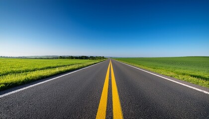Obraz premium panoramic view of a well maintained blacktop road with double yellow lines stretching through vibrant green fields under a clear blue sky