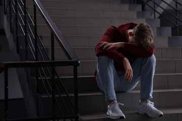 Bullying. Upset teenage boy on stairs indoors. Space for text