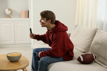 Emotional sports fan with remote control and ball watching game indoors