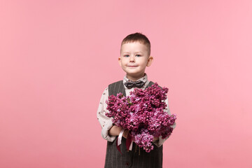 Little boy with bouquet of lilac flowers on pink background