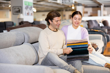positive young couple discussing collection of fabrics for furniture in apartment in furniture salon