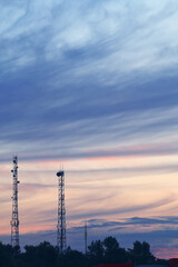 Summer Evening Landscape. A horizontal cityscape with two tall telecom towers near a town, set against a cloudy sunset sky after rain.