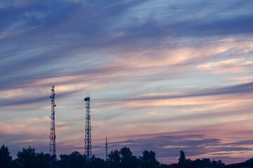 Summer Evening Landscape. A vertical cityscape with two tall telecom towers near a town, set against a cloudy sunset sky after rain.