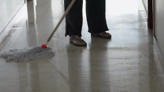 A woman mopping a shiny floor inside her apartment with flip-flops