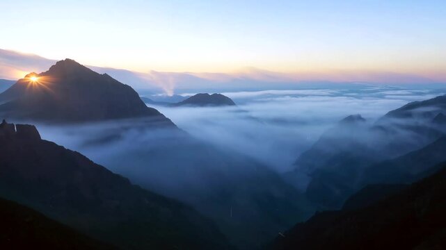  Mountains at dawn, shrouded in mist with soft light breaking through the clouds. The scene exudes tranquility and beauty, showcasing nature's artistry in the early morning glow.