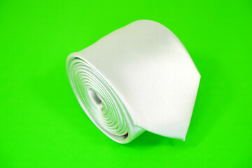 A plain fabric white tie rolled on green background , Tie macro photography 