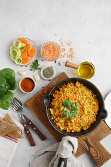 Red lentils dal in black pan and on plate on white table top. Lentils carrot and leek vegetarian meal, top vertical view, copy space