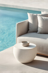 Modern outdoor lounge setting with minimalist round coffee table and neutral sofa by a clear blue swimming pool