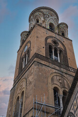 Obraz premium The bell tower of Amalfi Cathedral in Italy features Romanesque and Moorish details, colorful ceramic tiles, and scaffolding against a pink and blue sky.