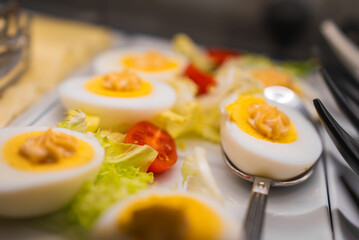 A plate of deviled eggs garnished with creamy filling, fresh lettuce leaves, and halved cherry tomatoes. Blurred utensils suggest a dining setting in Amalfi, Italy.