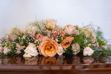 A floral arrangement of peach and blush roses, baby's breath, and greenery on a polished wooden...