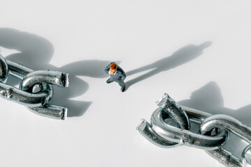 A miniature businessman figurine stands between the broken links of a metal chain. The scene suggests a concept related to business, security, or obstacles.