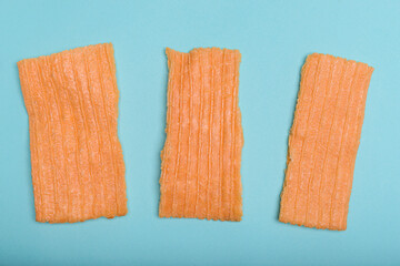 Three broken pieces of orange flour crackling are placed on a light blue background