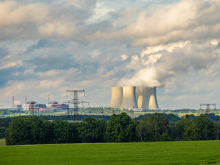 Nuclear power plant with cooling towers releasing steam into the sky, surrounded by lush green...