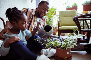 Father and daughter watering plants and flowers on the balcony of their apartment