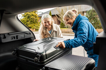 Senior caucasian lesbian couple packing their suitcase into the trunk of there car before going on a road trip vacation