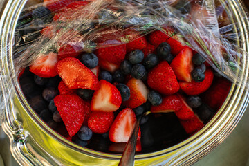 Strawberries and Blueberries in a bowl with plastic wrap on top 