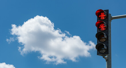 A traffic light showing red against a blue sky with a fluffy white cloud on a sunny day outdoors view