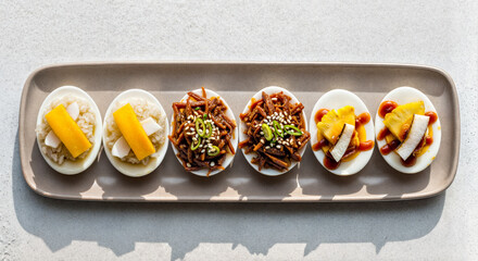 Top View of Three Eggs in Six Halves Decorated with Various Tasty Toppings on Rectangular Plate on White Surface in Bright Daylight 
