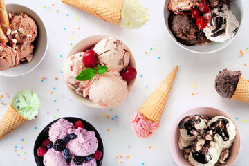 Summer ice cream table scene. Bowls and cones of colorful assorted flavors. Top view on a white marble background.