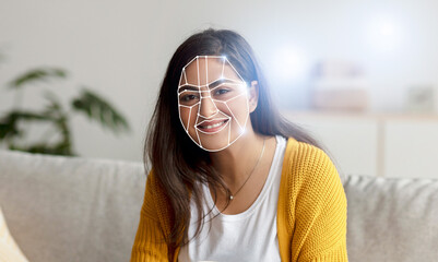 Indian woman sits on a couch with a smiling expression as facial recognition technology analyzes...