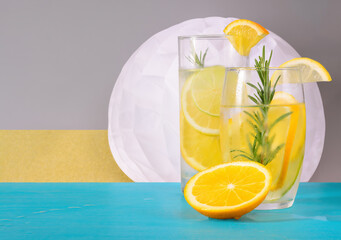 Two glasses of drink with lemons and a piece of orange on a gray background