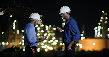 Two college Industrial engineer with white safety hat work with digital tablet and walkie talkie on night shift at Refinery and gas petrochemical plant, Industrial and business